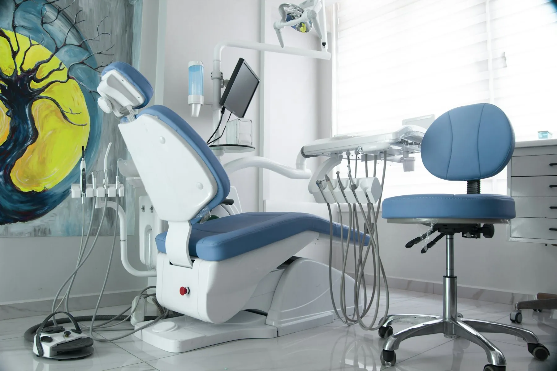 A modern treatment room with a blue dental chair and soft daylight