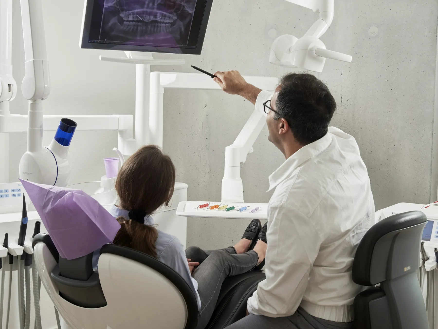 A dentist reviewing X-rays on a screen with a patient in the chair