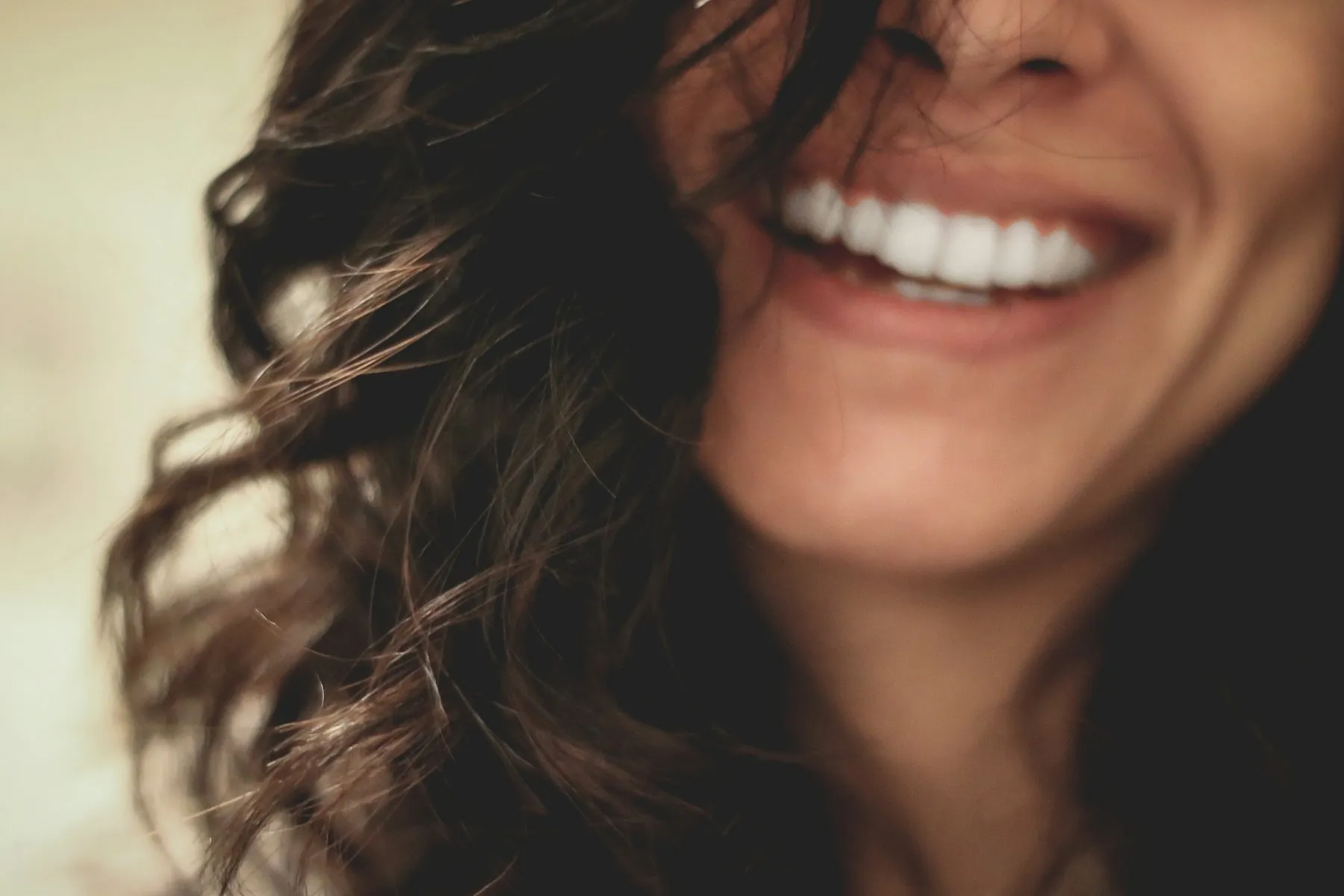 A woman with curly hair laughing, showing bright natural teeth